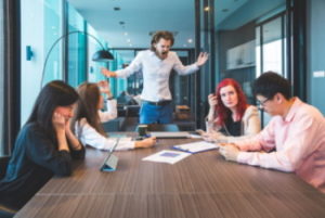Four team members are seating at the board room table with the fifth team member is standing and yelling - Positively People - family business conflict - Charleston, SC